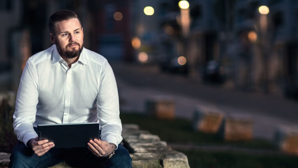 Andre ist Kundenberater bei AXA im Versicherungsvertrieb. Er sitzt auf einer Mauer und schaut in das Tablett auf dem die AXA eigene vertriebssoftware läuft