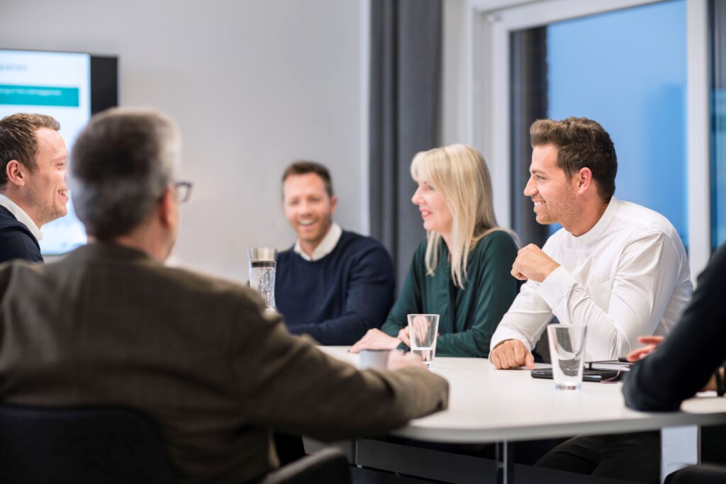 Quereinsteigerinnen und Quereinsteiger Versicherung und erfahrene Vertriebspartner und Vertriebspartnerinnen und Vertriebspartner im Gespräch in einer modernen AXA Agentur