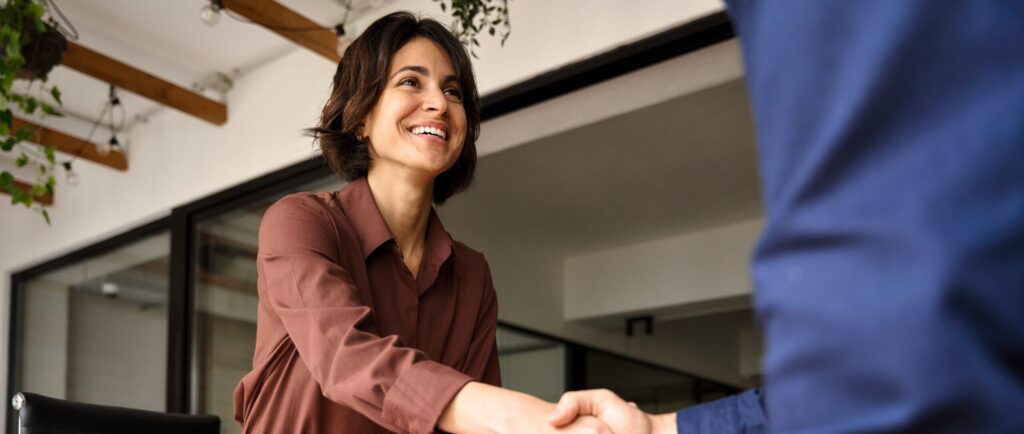 Quereinsteigerin begrüßt ihren neuen Vertragspartner mit einem Handschlag in einem modernen Büro